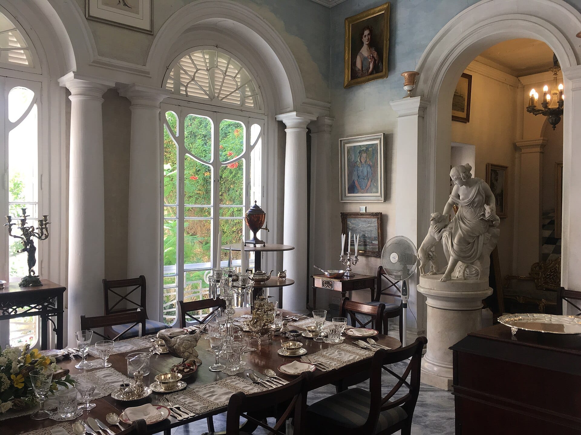 Elegante sala da pranzo di Casa Rocca Piccola, con tavola formale apparecchiata, statua classica, finestre ad arco e luce naturale che entra nella stanza.