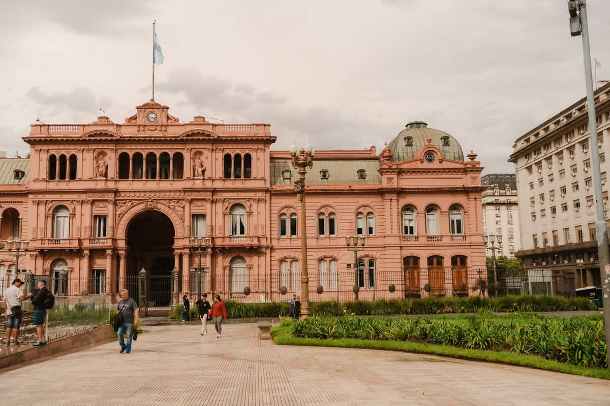 ด้านหน้าของ Casa Rosada ทำเนียบประธานาธิบดีอาร์เจนตินา ที่มีผู้คนเดินอยู่ในจัตุรัส และตัวตึกสีชมพูเด่นชัด