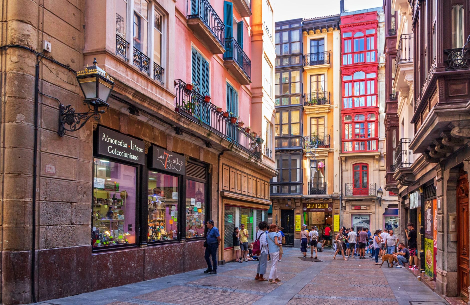 Pedestrian street in Bilbao’s Casco Viejo lined with colorful historic buildings, pintxos bars, and shops, with people walking and enjoying the vibrant medieval neighborhood atmosphere.