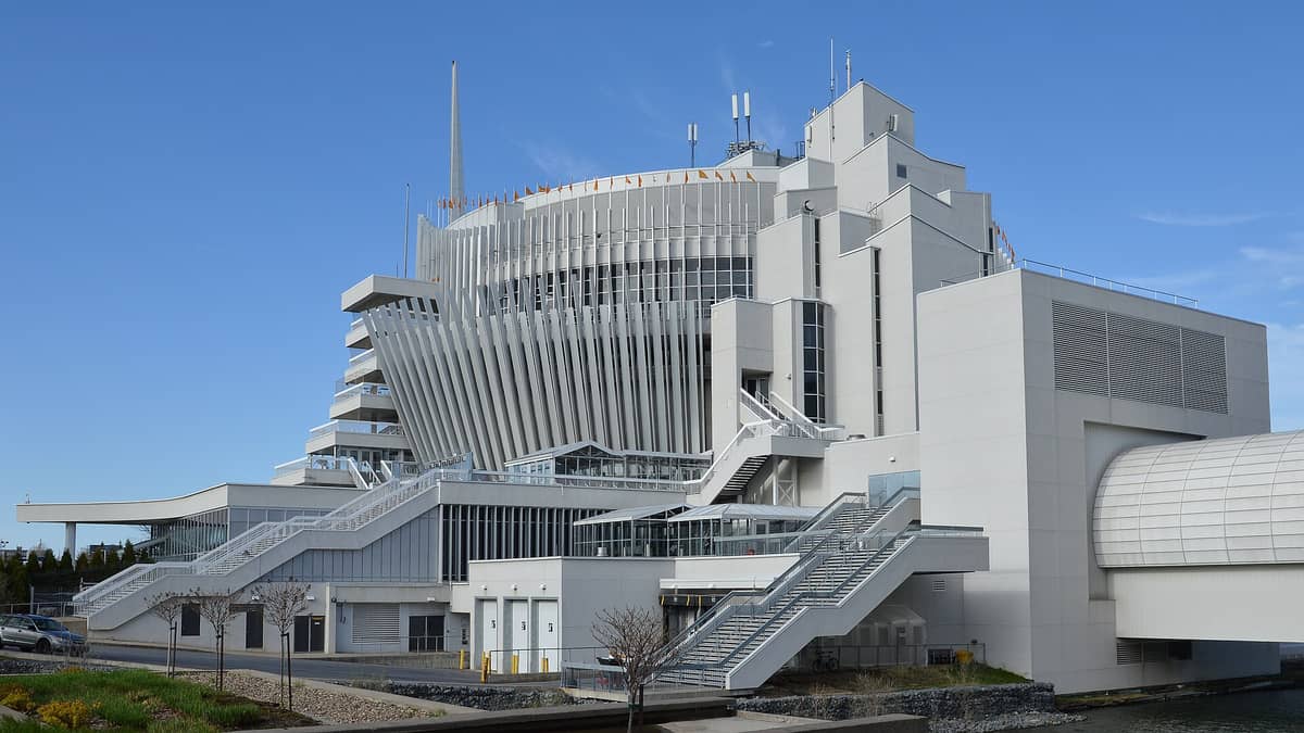 Außenansicht des Casino de Montréal: das markante weiße modernistische Gebäude mit ausgeprägten vertikalen Lamellen und Treppen unter strahlend blauem Himmel.