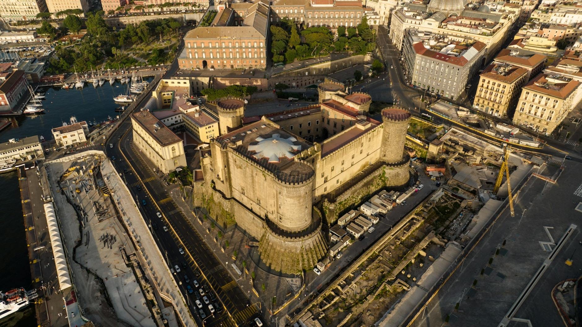 Vista aerea di Castel Nuovo (Maschio Angioino) con le sue cinque torri cilindriche che si ergono sul lungomare di Napoli, circondate dalle strade della città e dal porto.