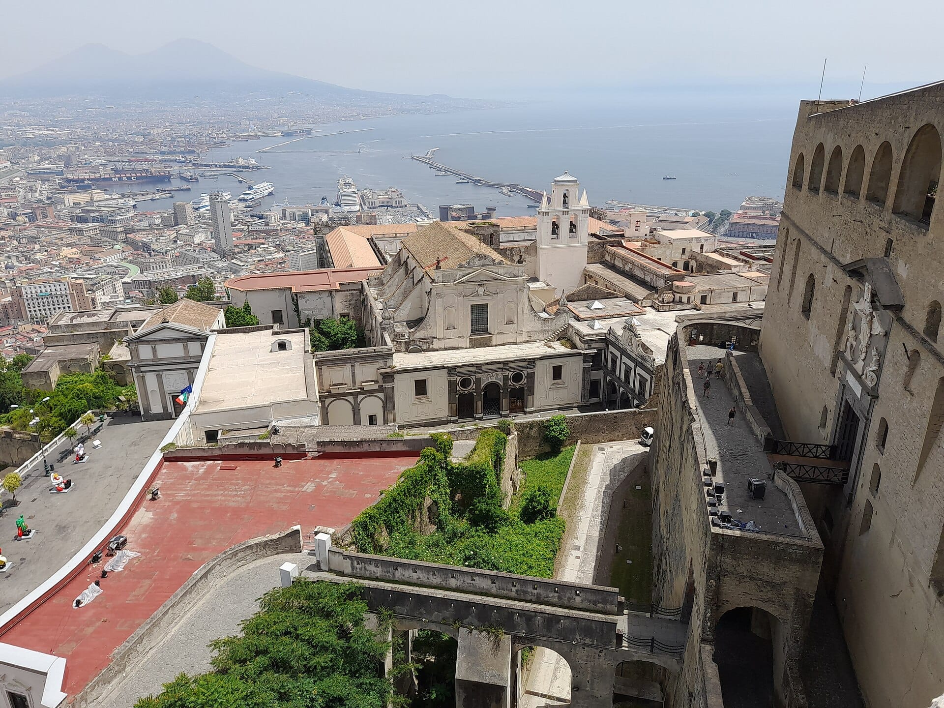 Vista da Castel Sant'Elmo su Napoli, il golfo e il Vesuvio sullo sfondo in una giornata serena, con le mura della fortezza in primo piano.