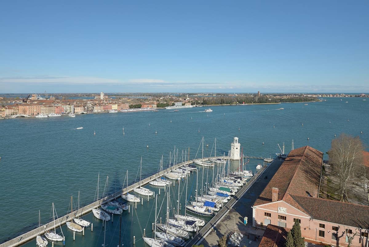 Luftaufnahme des gesamten Stadtviertels Castello in Venedig mit Blick auf die Uferpromenade, den Hafen, die bunten Häuser und Sant'Elena an der Spitze unter strahlend blauem Himmel.