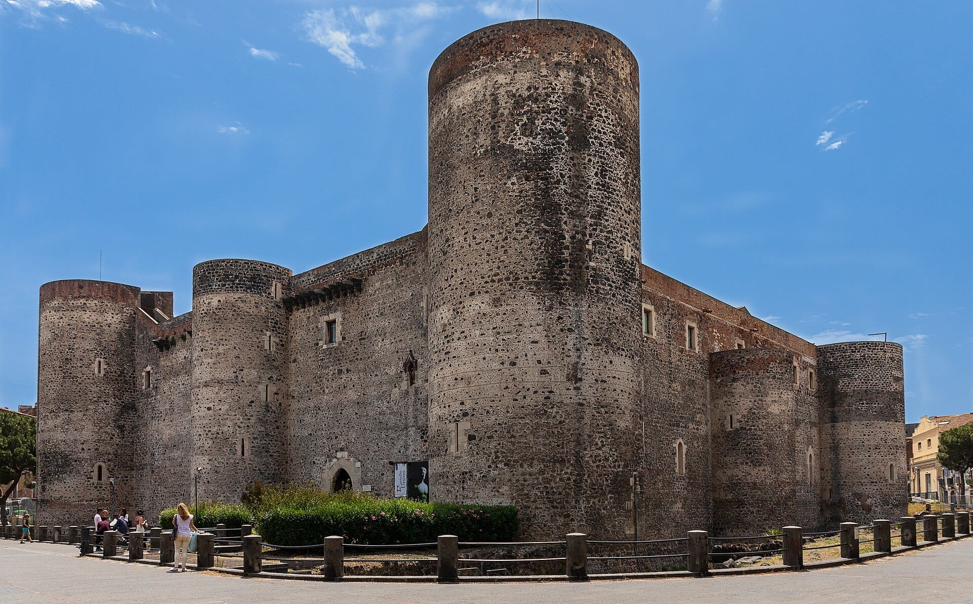 Die Steinmauern und runden Türme des Castello Ursino unter einem strahlend blauen Himmel, mit Besuchern, die in Catania in der Nähe spazieren und sitzen.