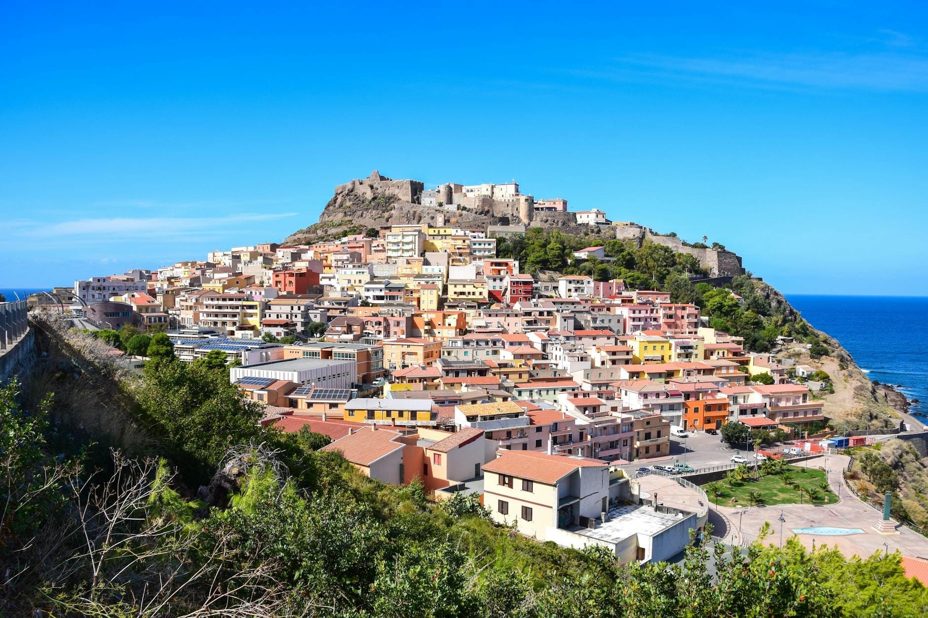 Panoramablick auf die Felsenstadt Castelsardo mit bunten Häusern und mittelalterlicher Festung über dem Meer an einem sonnigen Tag.