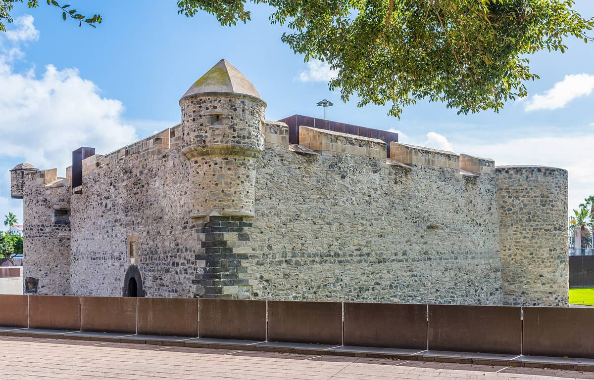 Вид сбоку на Castillo de la Luz — старейшую каменную крепость Гран-Канарии: округлая башня, каменные стены и синее небо над ними.