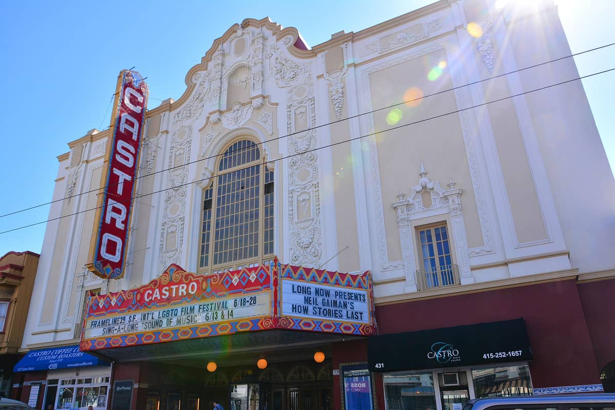La ornamentada fachada blanca de estilo barroco colonial español y el letrero vertical de neón rojo del Castro Theatre en San Francisco, con su colorido marquesino visible.