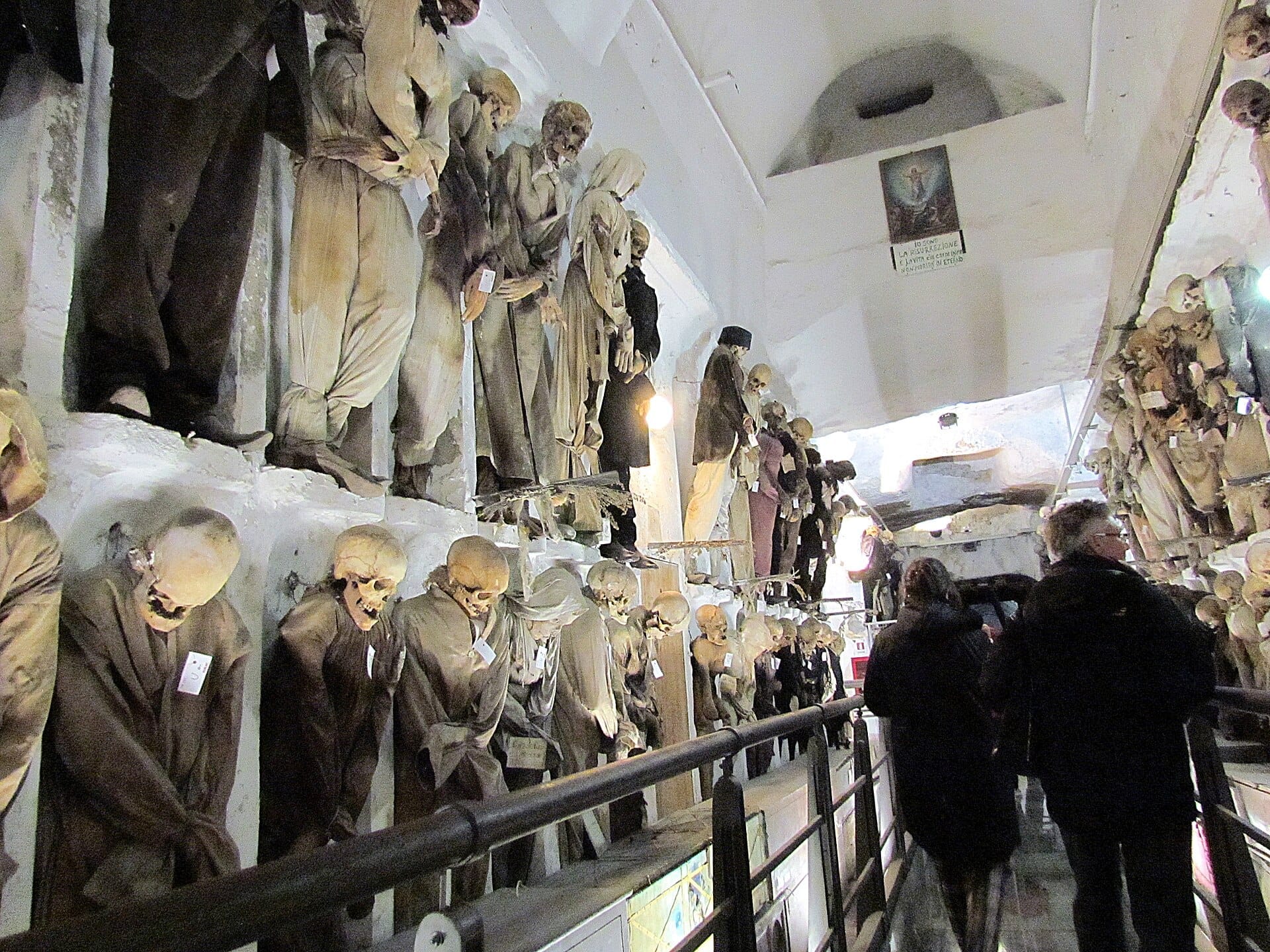 Reihen mumifizierter Körper in historischer Kleidung säumen die Steinwände der Kapuzinergruft von Palermo unter Gewölbedecken.