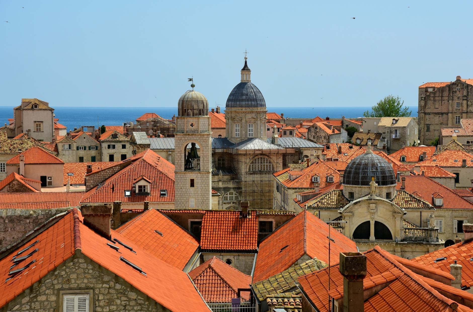 Vista panorámica del casco antiguo de Dubrovnik con la prominente cúpula barroca de la Catedral de la Asunción de la Virgen María destacando sobre los tejados de tejas rojas y el mar Adriático al fondo.