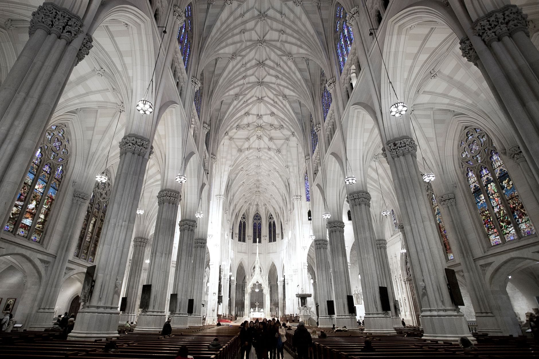 Vista dell'imponente interno di una grande cattedrale gotica, con soffitti a volta altissimi, colonne ornate e luminose vetrate colorate.