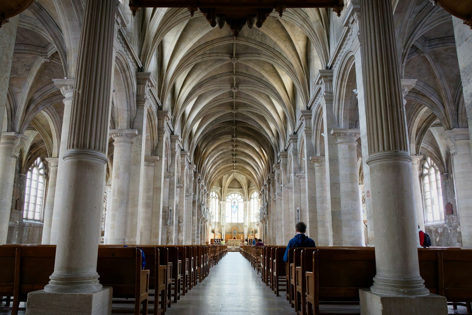 La luminosa navata in pietra di una cattedrale storica con archi a volta, luce che filtra da alte finestre e banchi in legno vuoti, a esaltare la bellezza senza tempo dell'architettura.