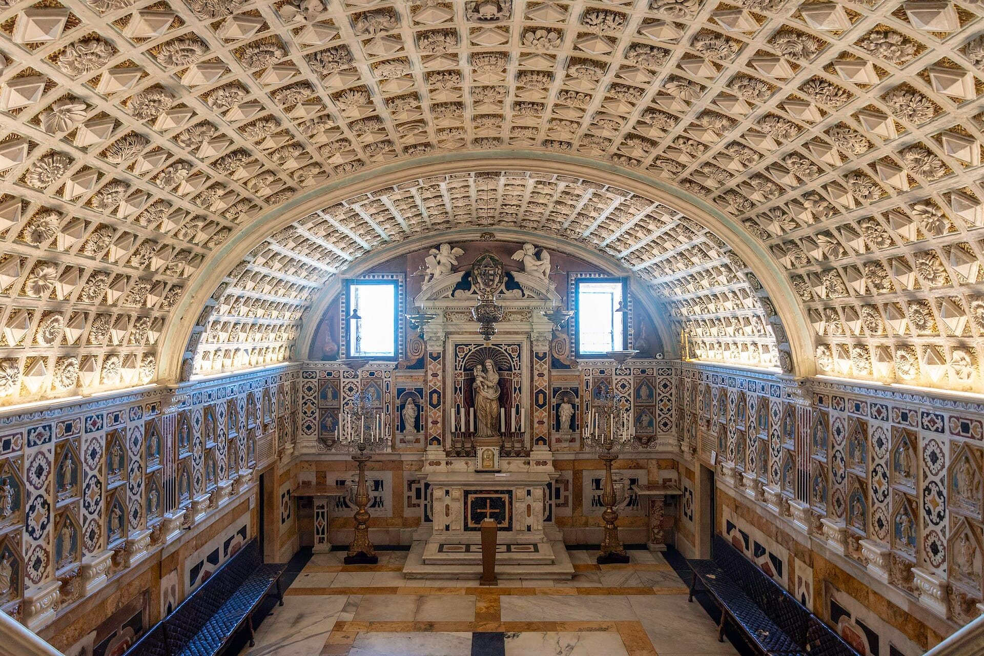 Kunstvoll verzierte Gewölbedecke und Marmoraltar im Inneren der Cattedrale di Santa Maria, Cagliari, mit symmetrischen Bänken und natürlichem Tageslicht.