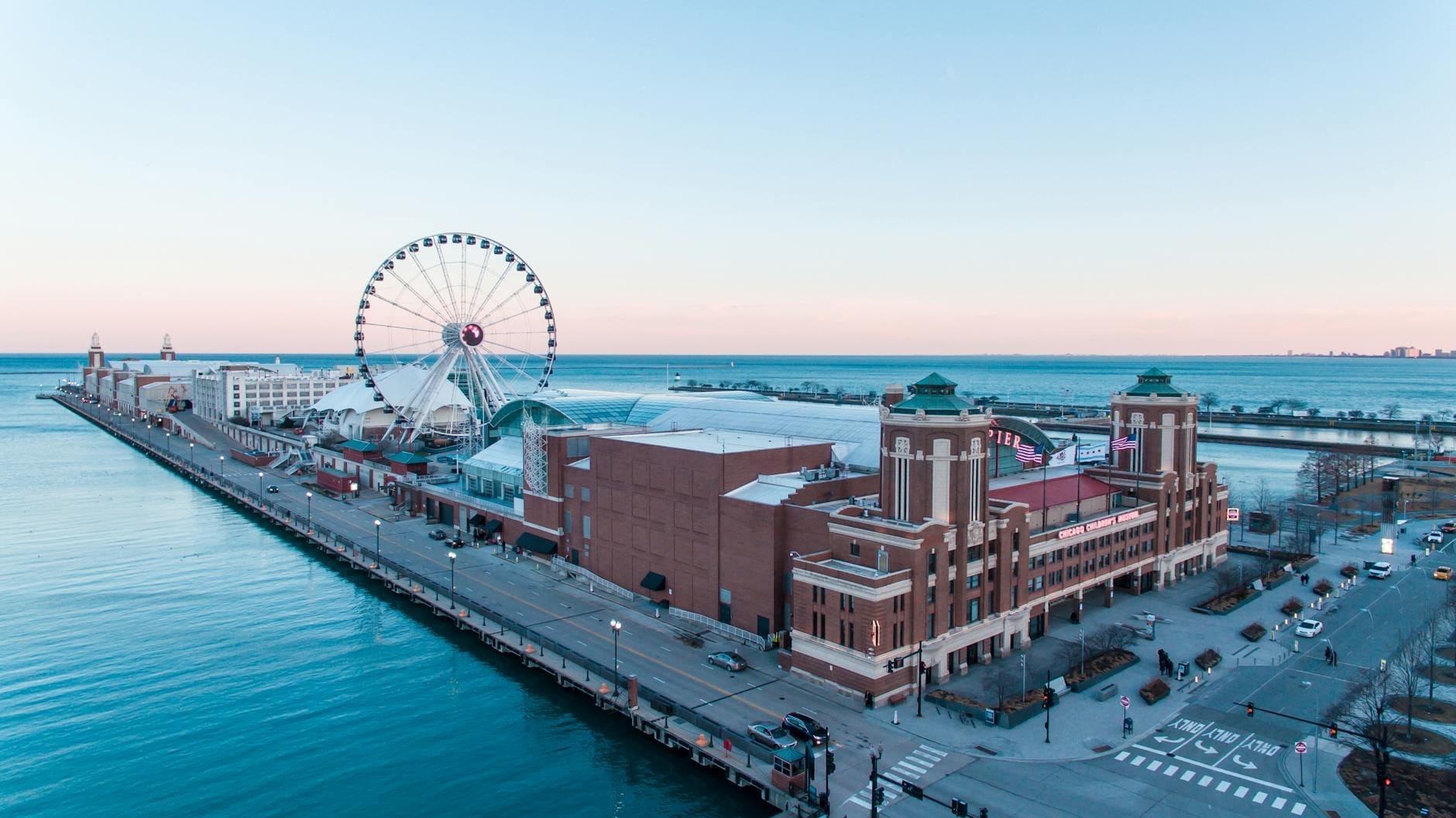 Vista aerea del Navy Pier con la Centennial Wheel in primo piano sullo sfondo del Lago Michigan e dello skyline di Chicago, ripresa di giorno con acqua e cielo di un azzurro nitido.