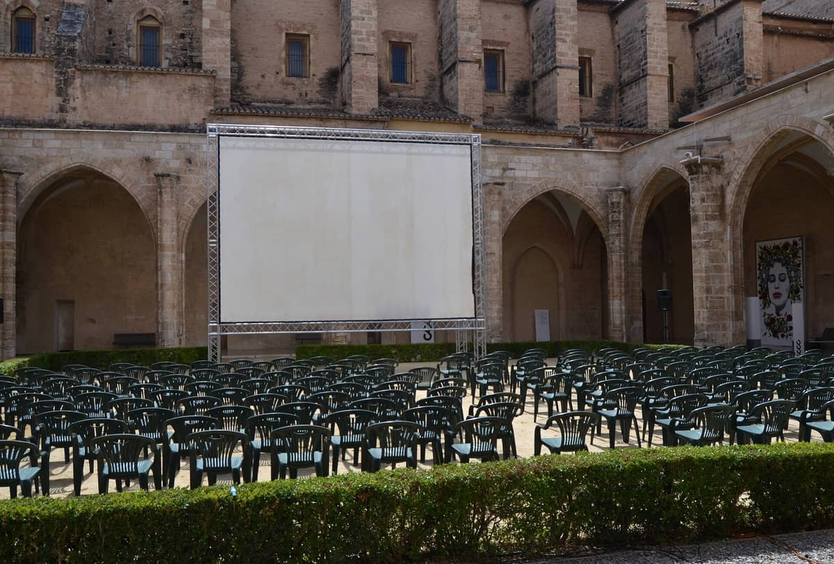 File di sedie di plastica vuote di fronte a uno schermo cinematografico all'aperto nel cortile medievale del Centre del Carme Cultura Contemporània.