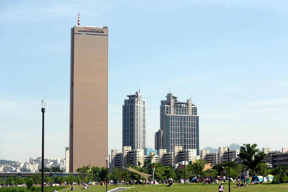 O Edifício 63, sede do Centre Pompidou Hanwha, ergue-se acima do horizonte de Yeouido num dia claro com um parque verde em primeiro plano.