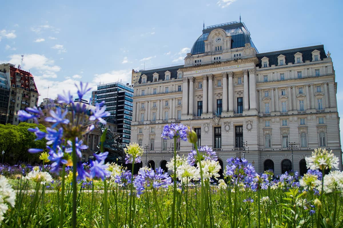ด้านหน้าอาคารสไตล์นีโอคลาสสิกของ Centro Cultural Kirchner (CCK) ในบัวโนสไอเรส มุมต่ำมีดอกไม้และท้องฟ้าสีฟ้าอยู่ด้านหน้า
