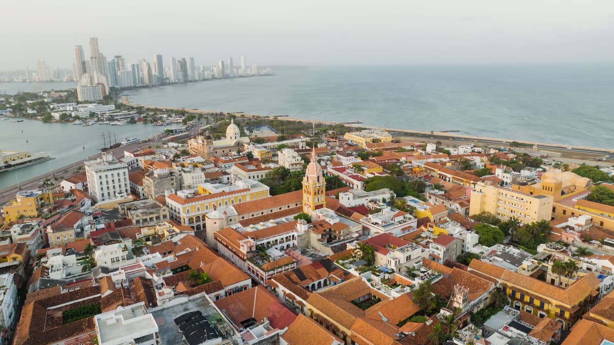 Aerial view of Cartagena's Centro Histórico, showing the walled city, colonial buildings, the cathedral, and the Caribbean Sea with Bocagrande skyline in the background.