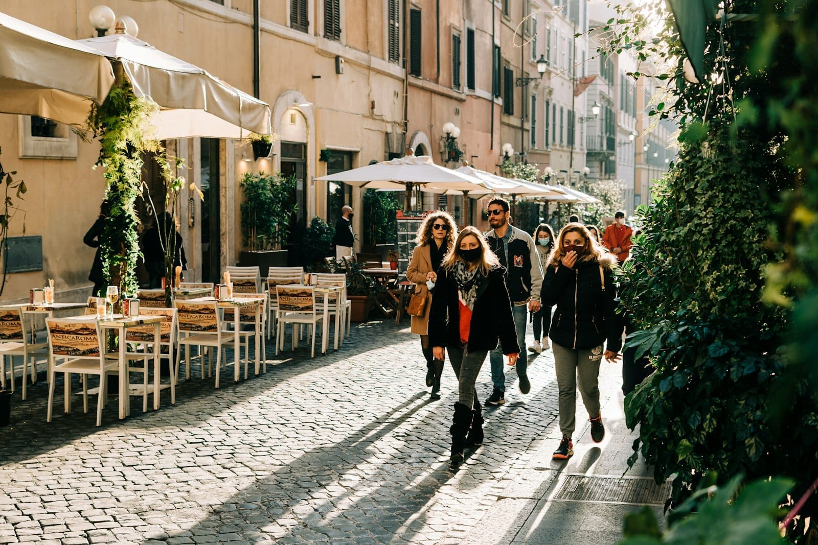 People walking on a sunlit cobblestone street with outdoor cafes and historic buildings in Rome’s Centro Storico, capturing its vibrant daily life and charm.