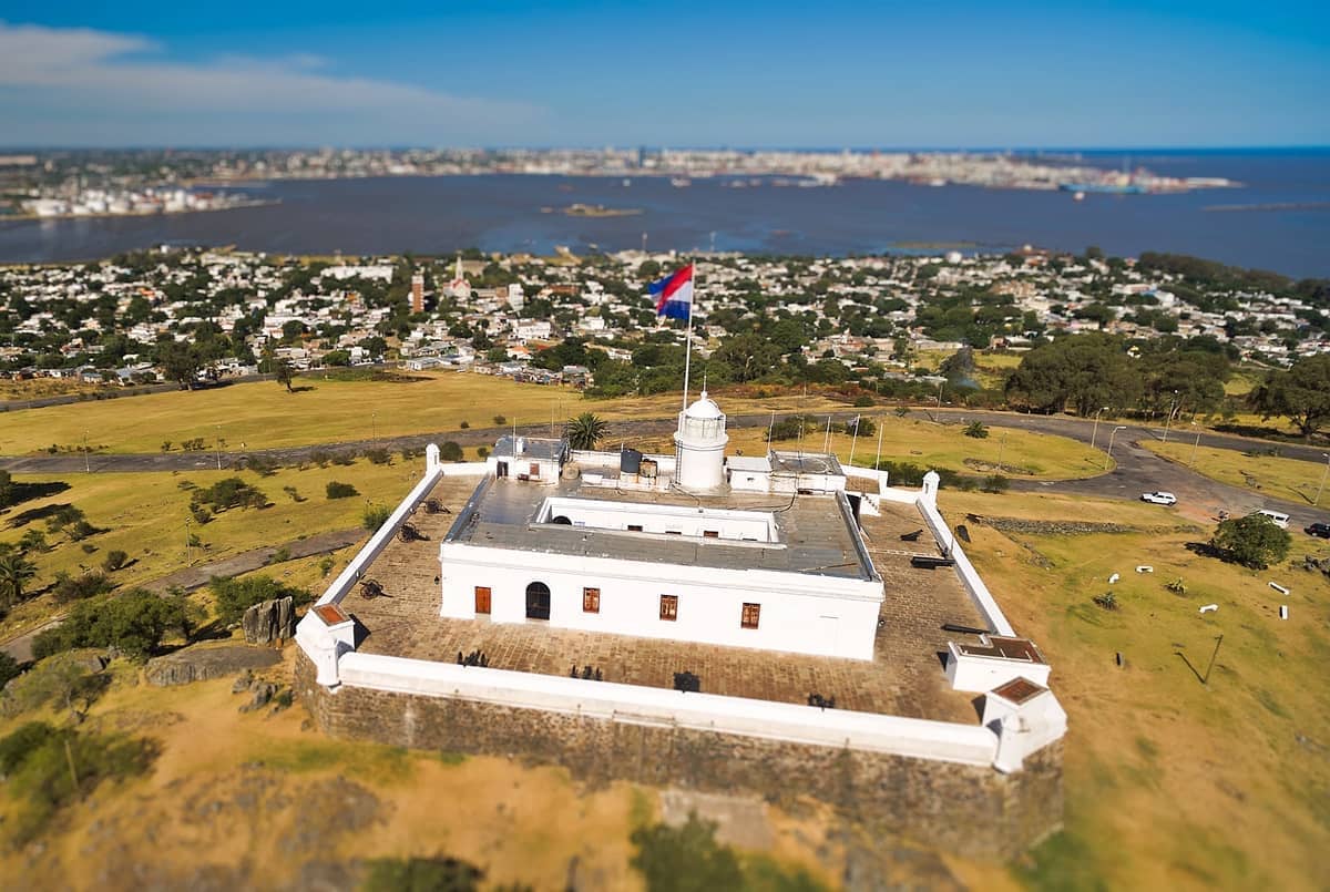 มุมมองทางอากาศของ Fortaleza General Artigas บนยอด Cerro de Montevideo ล้อมรอบด้วยทุ่งหญ้า โดยมีทิวทัศน์เมืองและอ่าวเป็นฉากหลัง