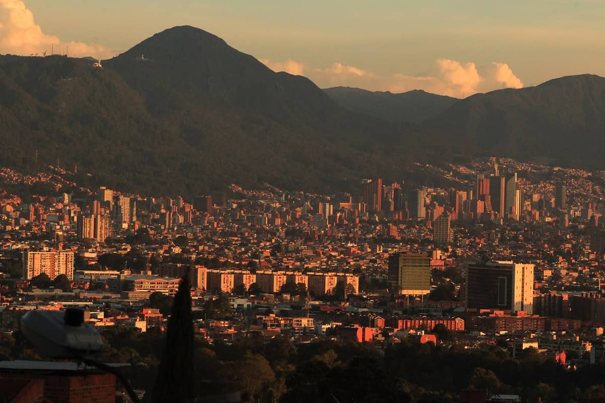 Wide view of Bogotá city with the forested Cerros Orientales mountains forming a dramatic eastern backdrop at sunset.