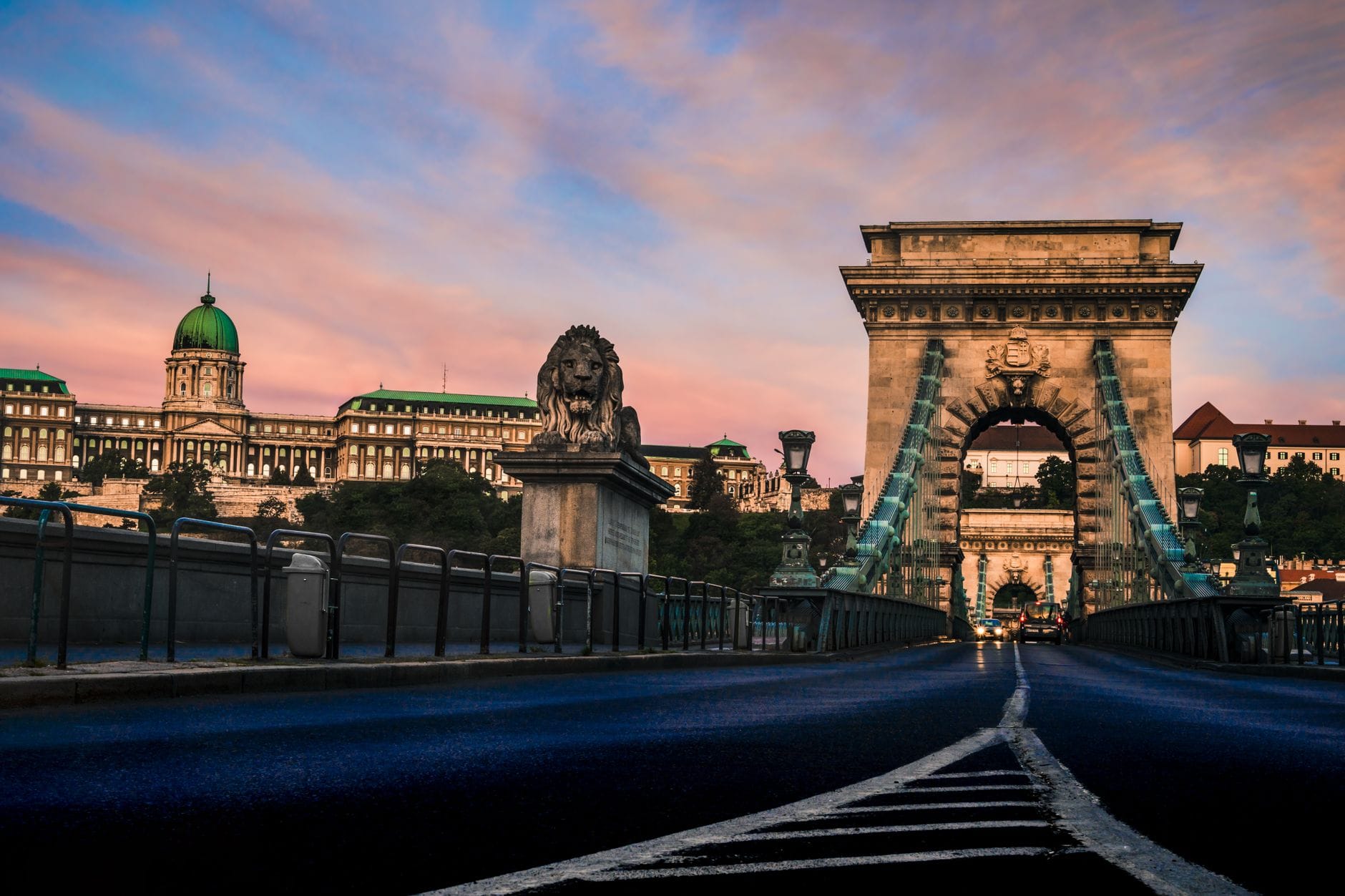 Vista dal basso del Ponte delle Catene Széchenyi al tramonto con cielo vivace, che mostra i leoni in pietra, la struttura del ponte e il Castello di Buda sullo sfondo.