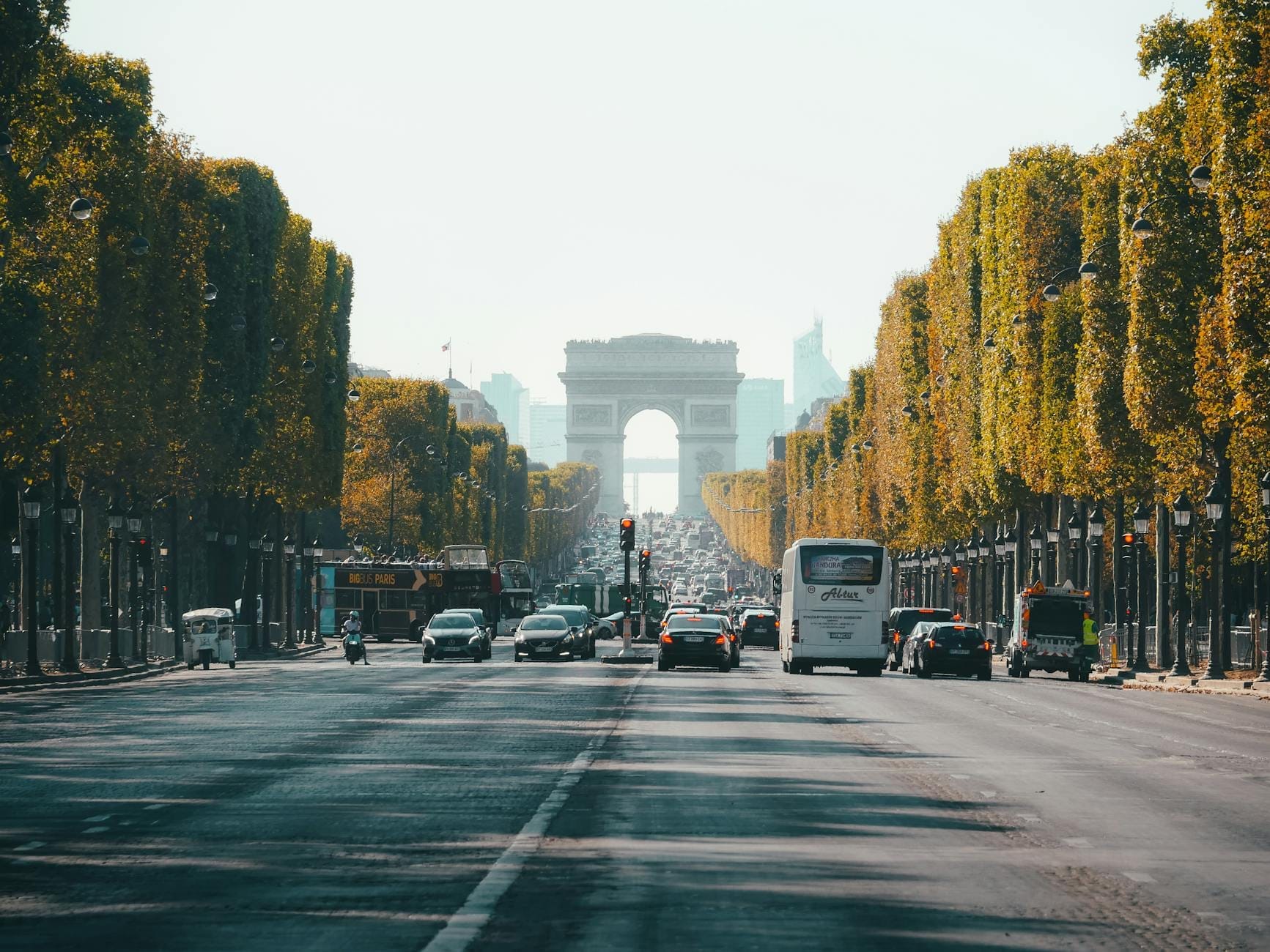 Una vista ampia lungo i Champs-Élysées, fiancheggiati da alberi e traffico, con l'Arc de Triomphe in lontananza in una giornata limpida.