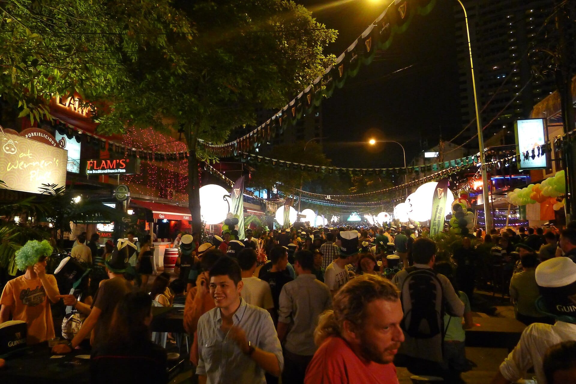 Crowds gather at night on Changkat Bukit Bintang under festive lights, surrounded by lively bars, trees, and bustling street decorations.