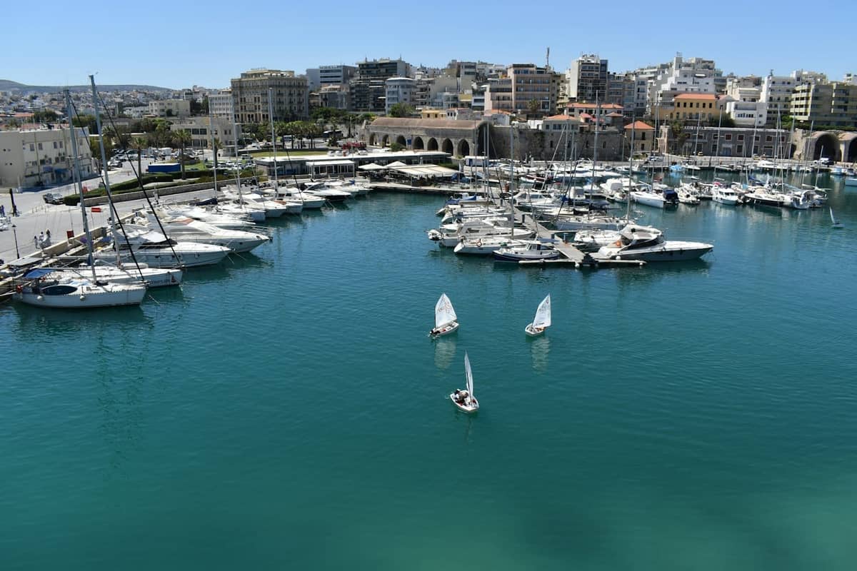 Widok na marinę Heraklion z nowoczesnymi budynkami miejskimi, łodziami i jachtami. Miejska scena nadmorska pod bezchmurnym błękitnym niebem.