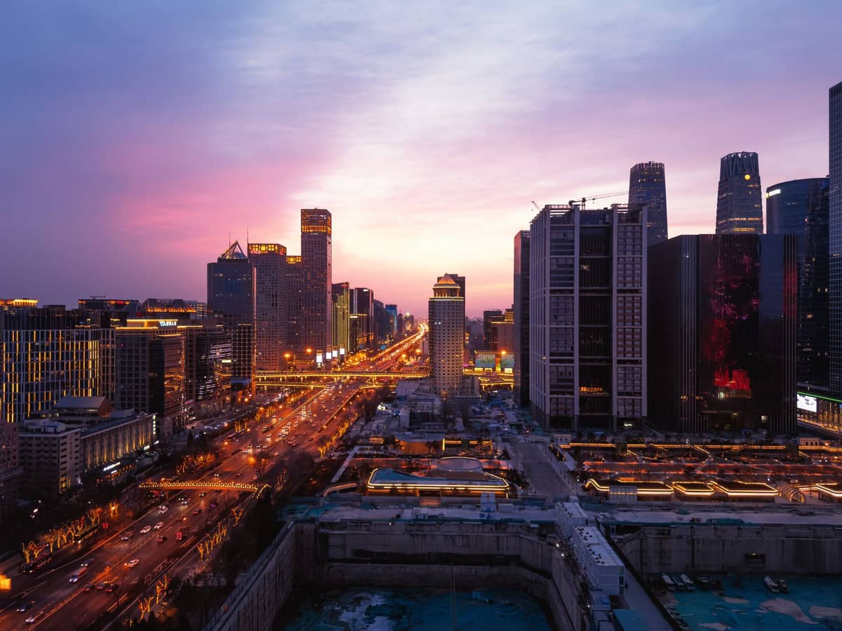 Weiter Blick bei Sonnenuntergang auf die Skyline des Pekinger Central Business District in Chaoyang, mit beleuchteten Wolkenkratzern und Stadtstraßen, die die moderne städtische Atmosphäre des Bezirks zeigen.