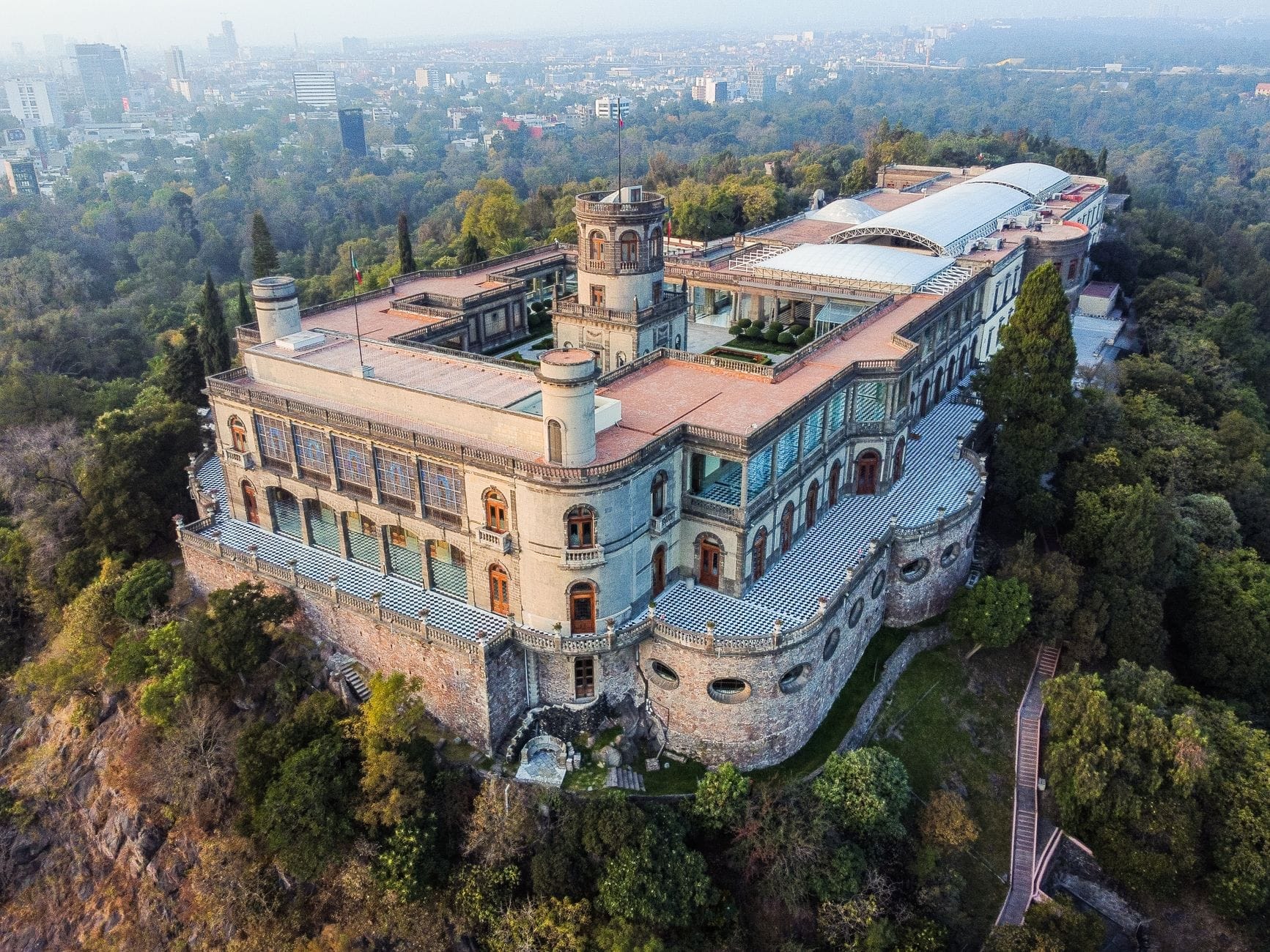 Vista aerea del Castello di Chapultepec arroccato su una collina, circondato dal verde con una vista panoramica su Città del Messico sullo sfondo.