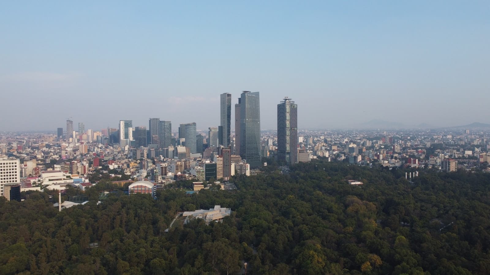 ภาพถ่ายมุมสูงเมืองเม็กซิโกซิตี้ เห็นผืนป่าสีเขียวของ Bosque de Chapultepec ด้านหน้า และเส้นขอบฟ้าของโปลังโกยุคใหม่เบื้องหลังในวันที่อากาศปลอดโปร่ง