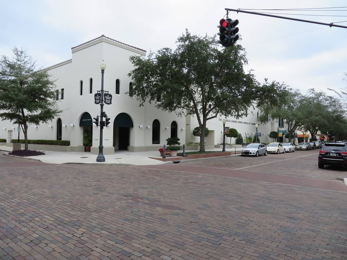 Das Charles Hosmer Morse Museum of American Art zeigt ein weißes Stuckgebäude mit Bogenfenstern und grünen Markisen entlang einer baumgesäumten Straße.