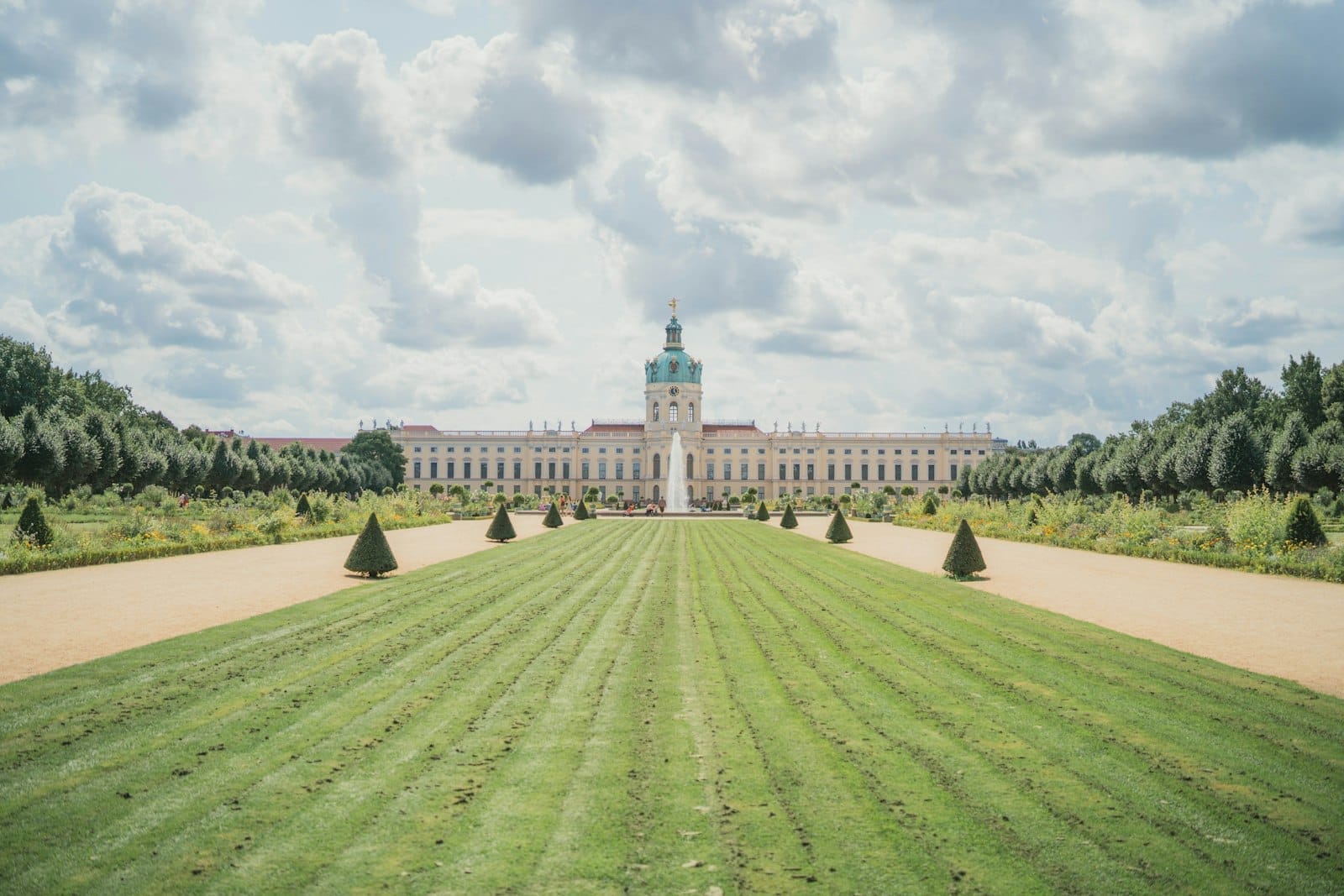 มุมกว้างของพระราชวัง Charlottenburg สนามหญ้าเรียบเรียง ทางเดินสมมาตร มีต้นไม้และท้องฟ้ามีเมฆบางส่วนในเบอร์ลิน