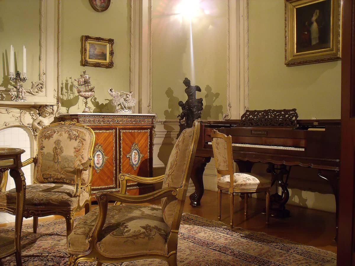 Prunkvoller Salon im Château Dufresne in Montréal mit aufwendigen historischen Möbeln, einem Konzertflügel und üppiger Beaux-Arts-Dekoration an den Wänden.