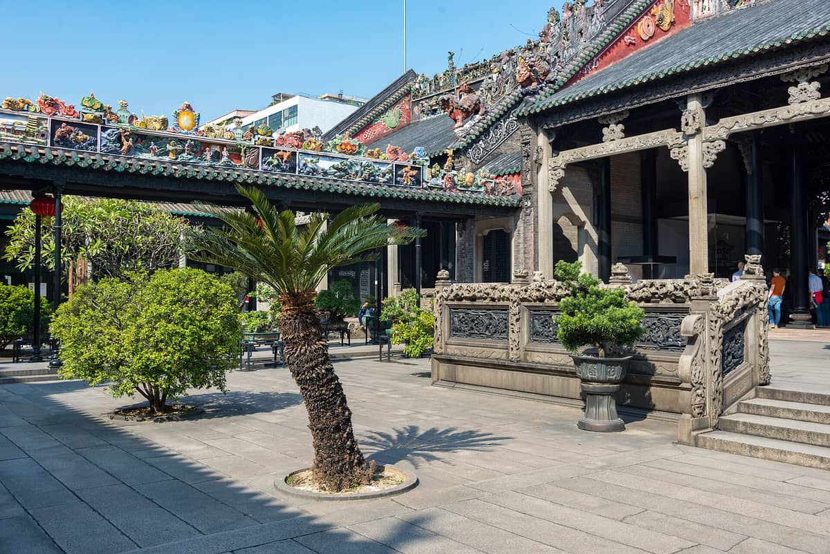 Courtyard of the Chen Clan Ancestral Hall showing ornate rooflines, colorful ceramic friezes, stone carvings, and lush garden plants in Guangzhou.
