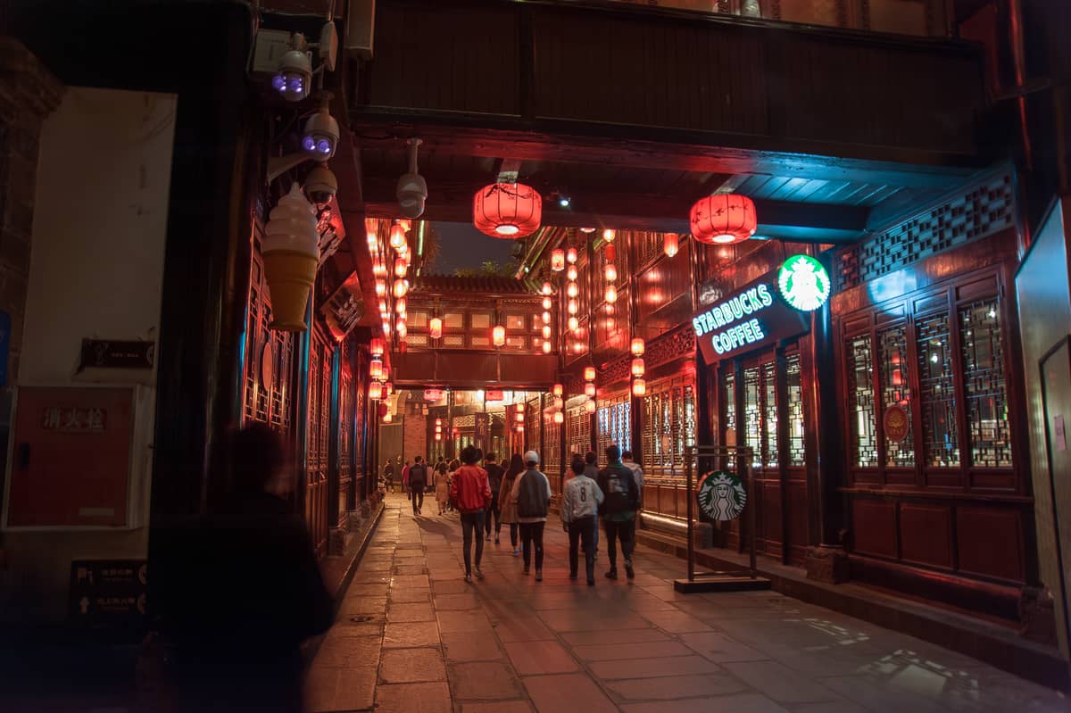 Escena nocturna de una calle antigua de Chengdu con personas caminando bajo faroles rojos, edificios tradicionales e iluminación acogedora y romántica.