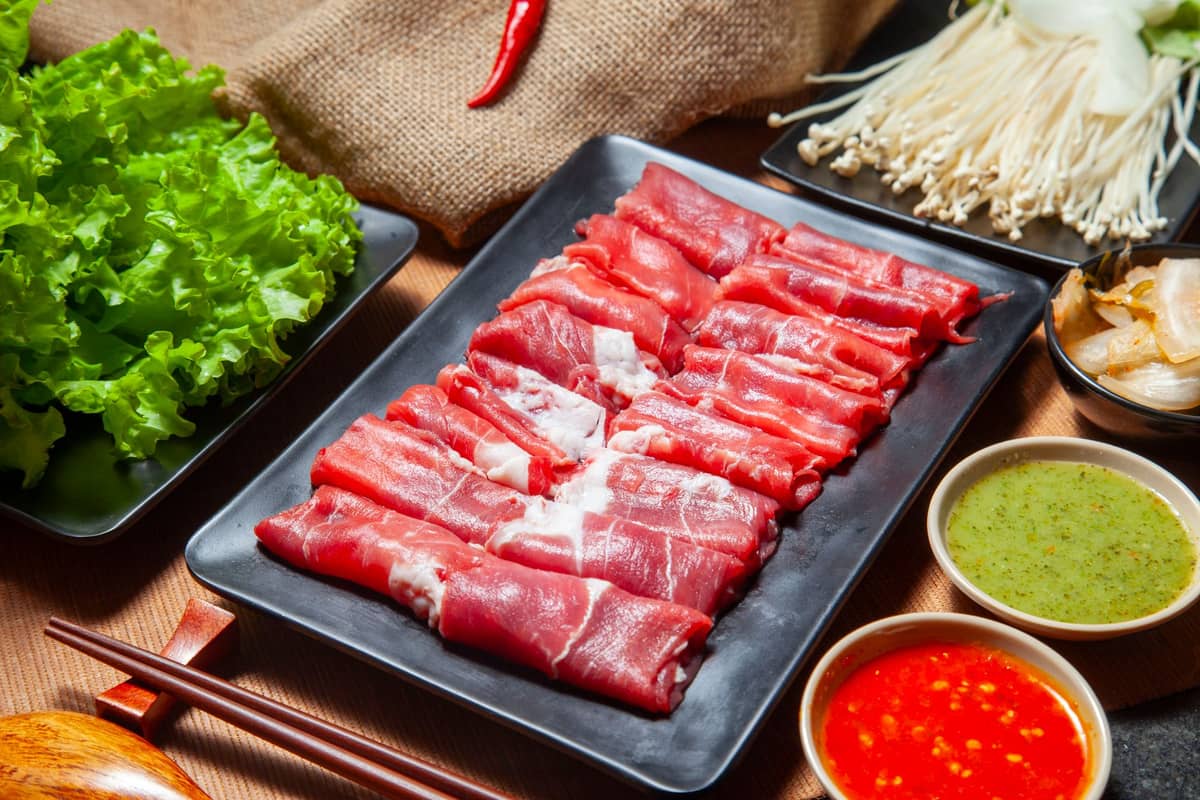 Un vassoio con manzo affettato sottilmente, salse per intingere, lattuga, funghi e altri ingredienti di hot pot disposti su un tavolo.