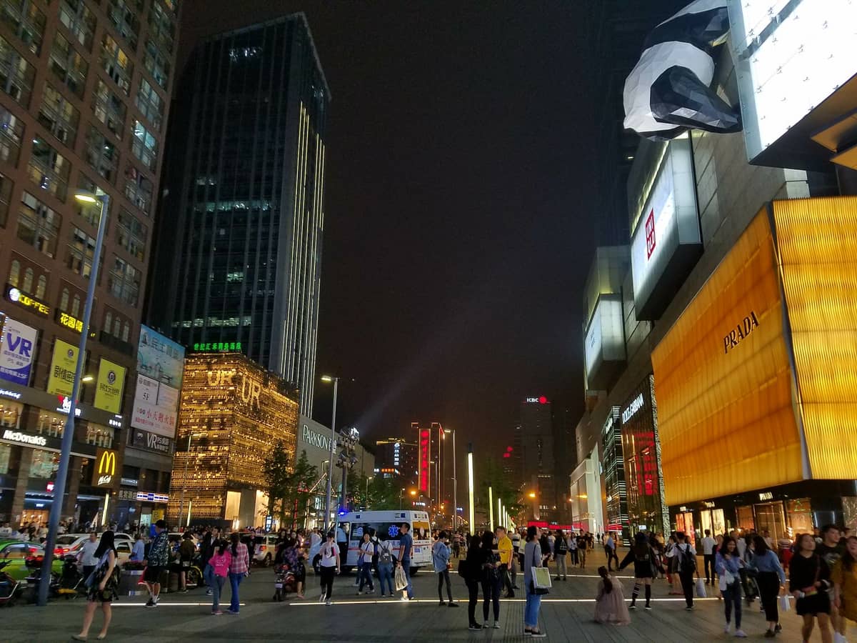 Vista notturna della vivace strada commerciale all'aperto del centro commerciale IFS di Chengdu, con folla, vetrine illuminate e iconici brand del lusso.