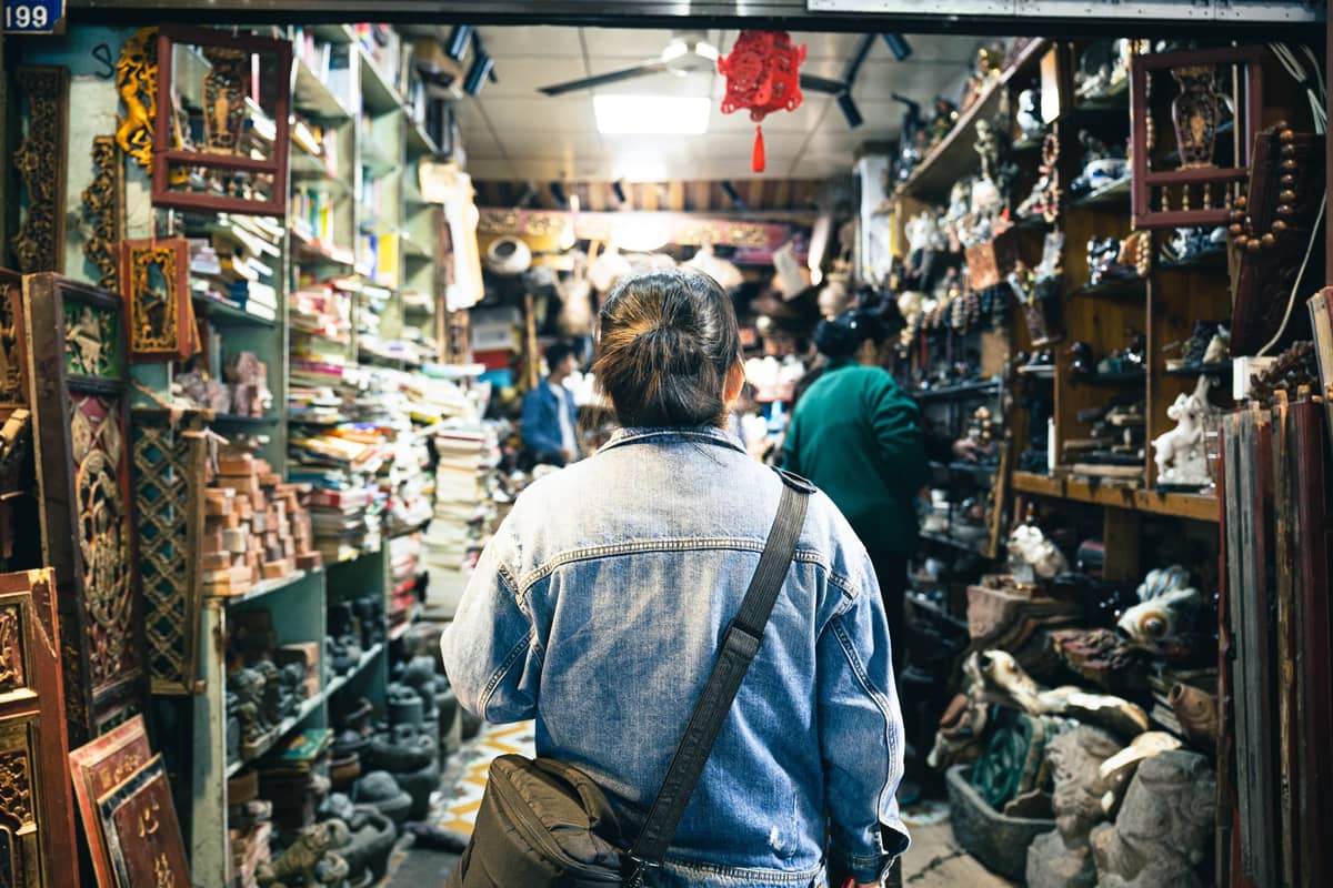 Persona che esplora una bancarella di mercato al coperto, affollata e stretta in Cina, piena di antichità e curiosità sugli scaffali.