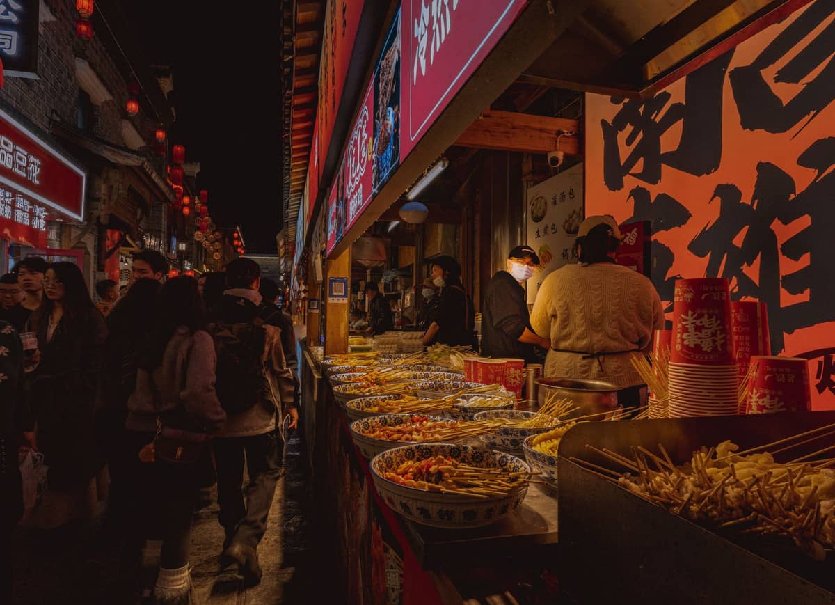Makulay na tindahan ng street food sa gabi sa Chengdu na may mga ihaw, parol, at mga pamilyang dumadaan, mga nagtitinda ng sikat na meryenda ng Sichuan sa ilalim ng maliwanag na karatula.