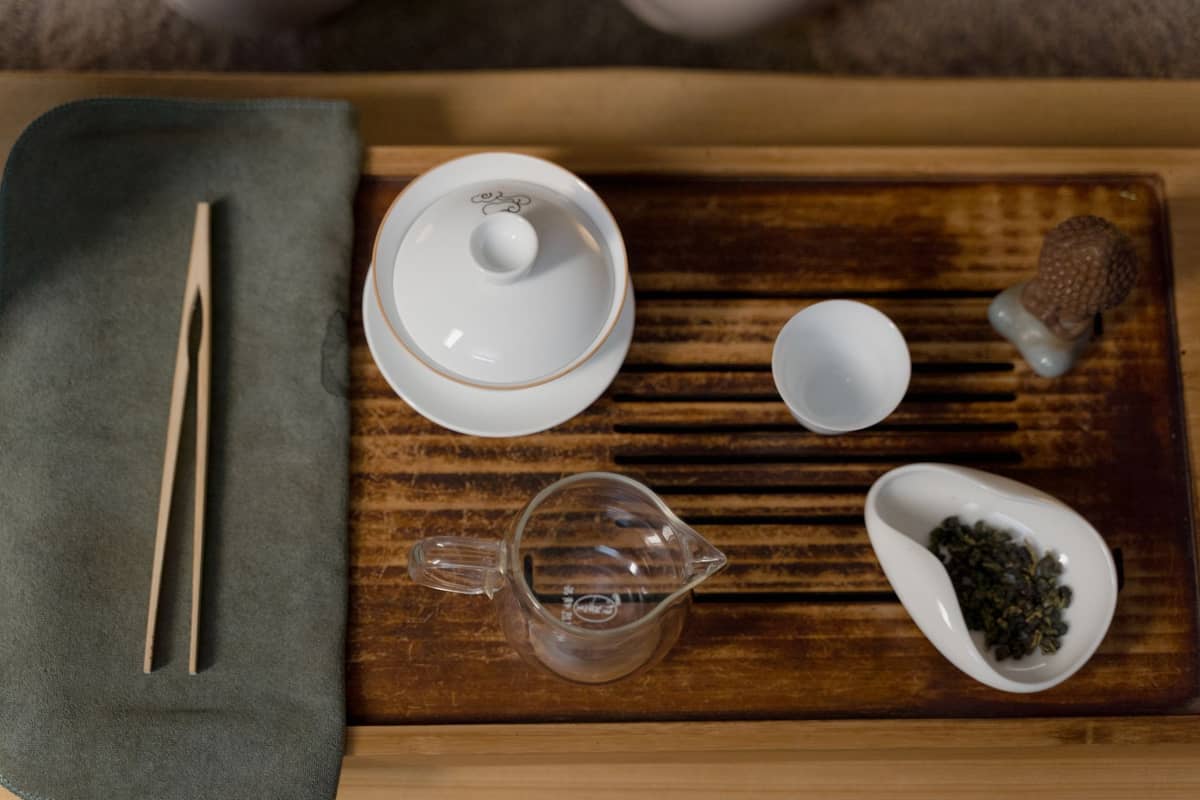 Draufsicht auf ein Gaiwan-Teeservice auf einem Holztablett mit Teeblättern und Utensilien, bereit zur Zubereitung.