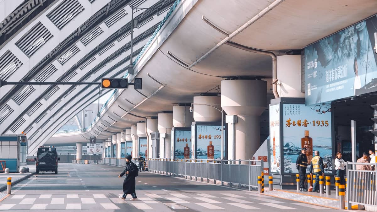 Menschen, die entlang eines großen überdachten Gehwegs neben einer modernen Überführung in Chengdu spazieren, mit sichtbaren Schildern und Eingängen.
