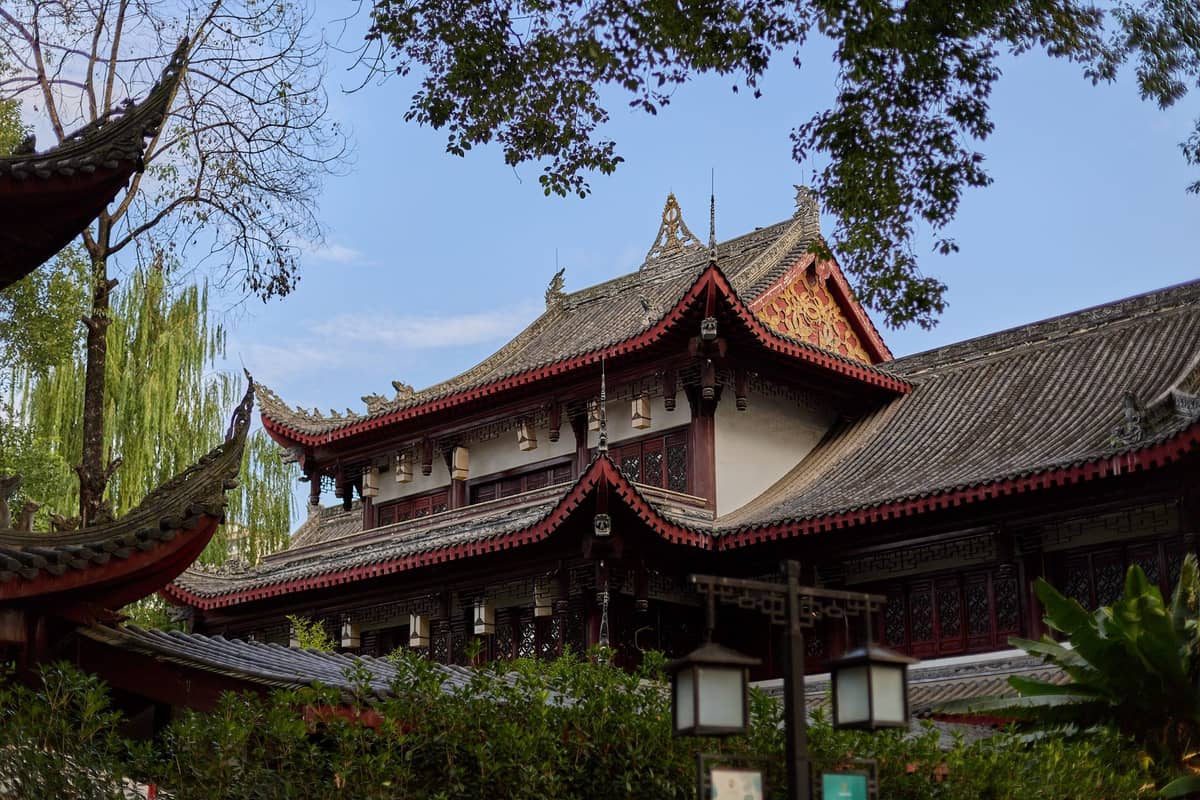 Traditionelle chinesische Tempelgebäude, umgeben von grünen Bäumen unter einem klaren blauen Himmel in Chengdu.