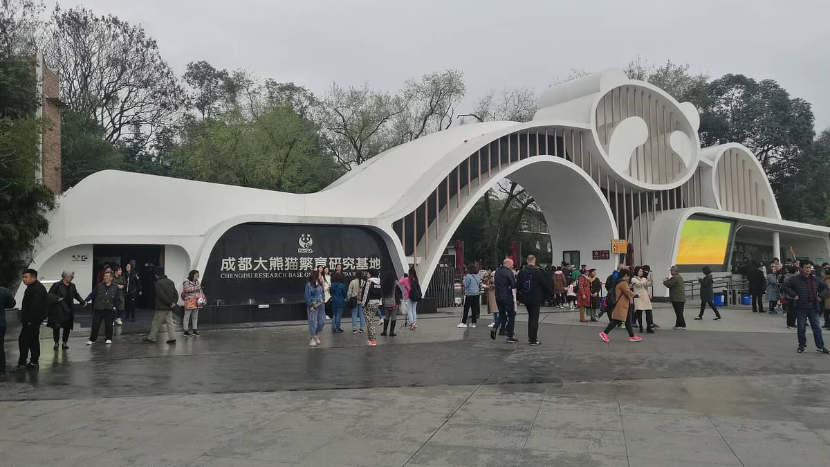 Weitwinkelansicht des Haupteingangs der Chengdu Research Base of Giant Panda Breeding mit Besuchermassen und der ikonischen Panda-Kopf-Architektur.