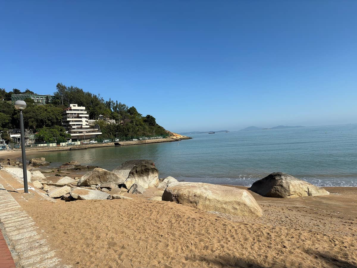 Cheoc Van Beach mit goldenem Sand, großen Felsen entlang des Ufers, ruhigem blauem Meer und modernen Gebäuden eingebettet in üppige grüne Hügel.