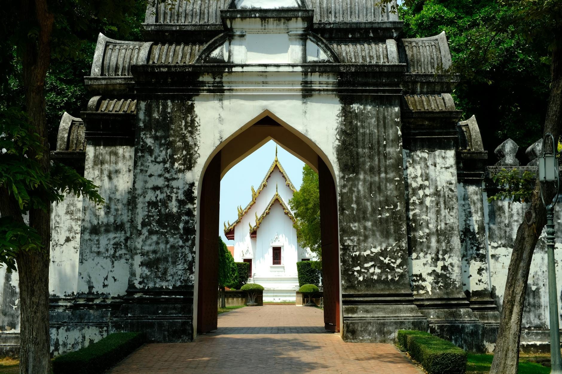 Histórica entrada blanca con arco y vista de un edificio patrimonial detrás, rodeada de vegetación en Chiang Mai.