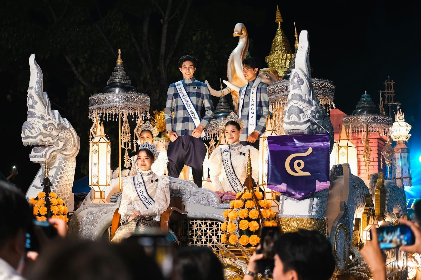 Carroza elaboradamente decorada en el Festival de las Flores de Chiang Mai con personas en trajes tradicionales y vibrantes decoraciones florales por la noche.
