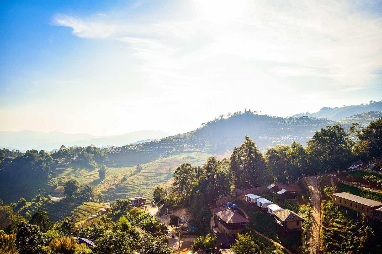 Aldea de montaña iluminada por el sol con colinas verdes, parcelas agrícolas y casas tradicionales cerca de Chiang Mai, perfecta para excursiones de un día con paisajes pintorescos.