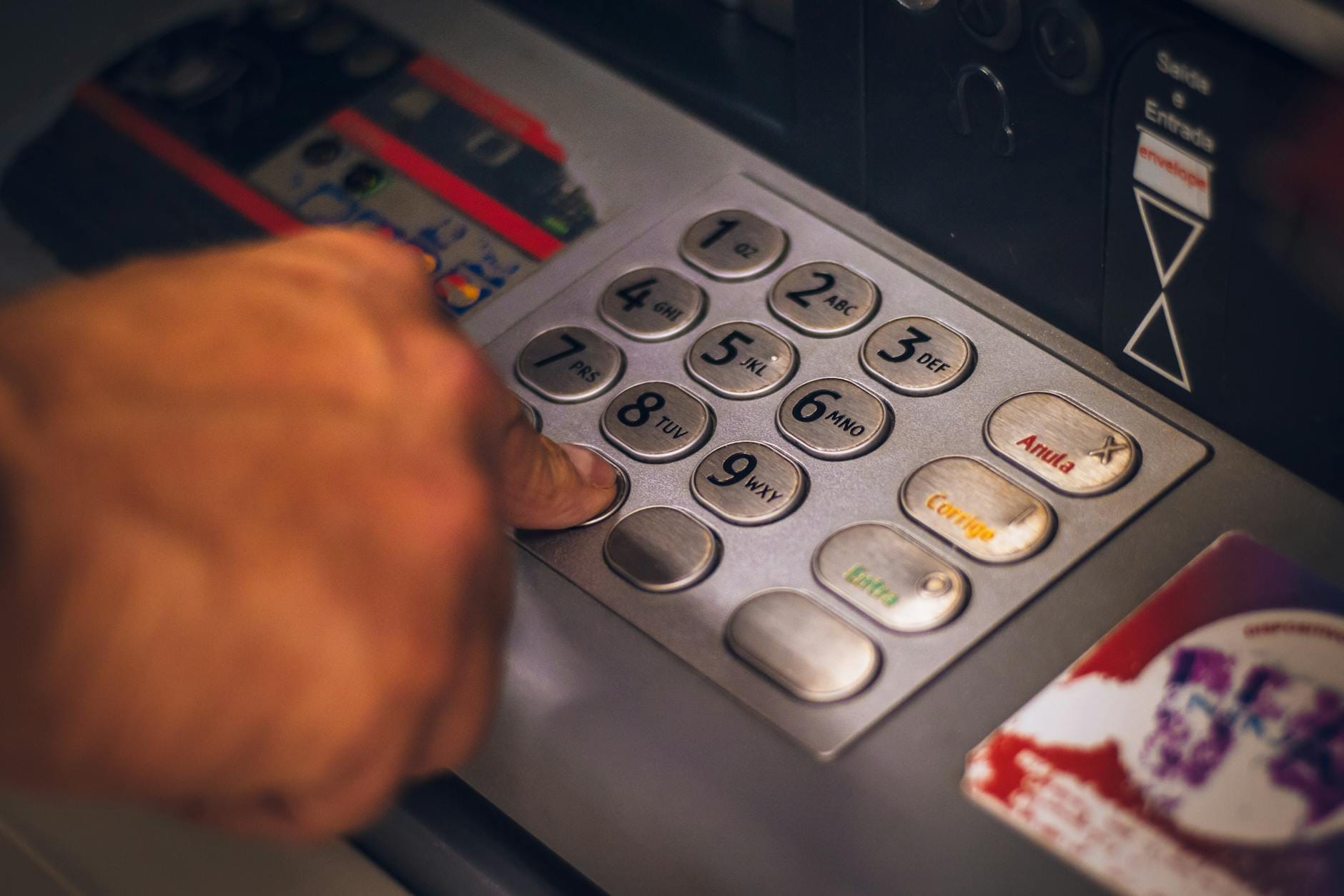 La mano de una persona presionando los botones del teclado de un cajero automático, destacando el acceso a efectivo y tarjetas en Tailandia.