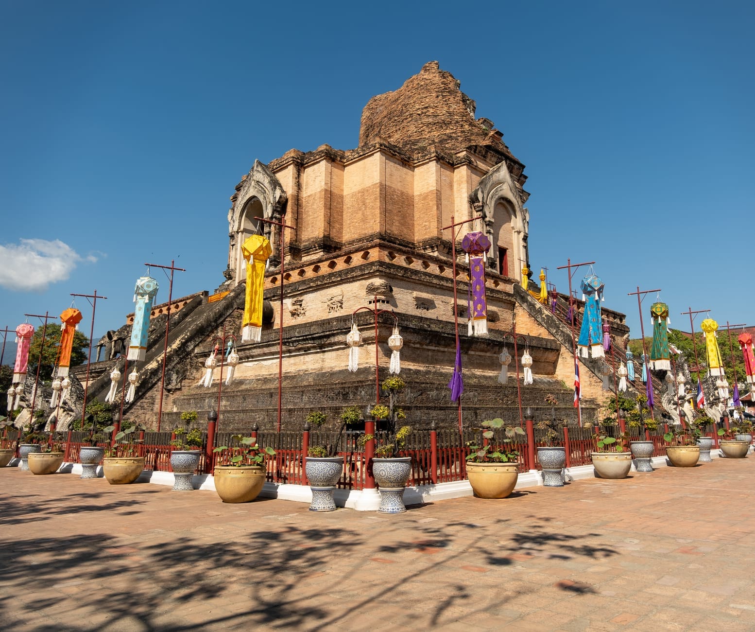 Vista amplia de la antigua estupa de ladrillo de Wat Chedi Luang con coloridas banderas de templo y cielo azul despejado, mostrando el icónico monumento de la Ciudad Antigua de Chiang Mai en plena luz del día.